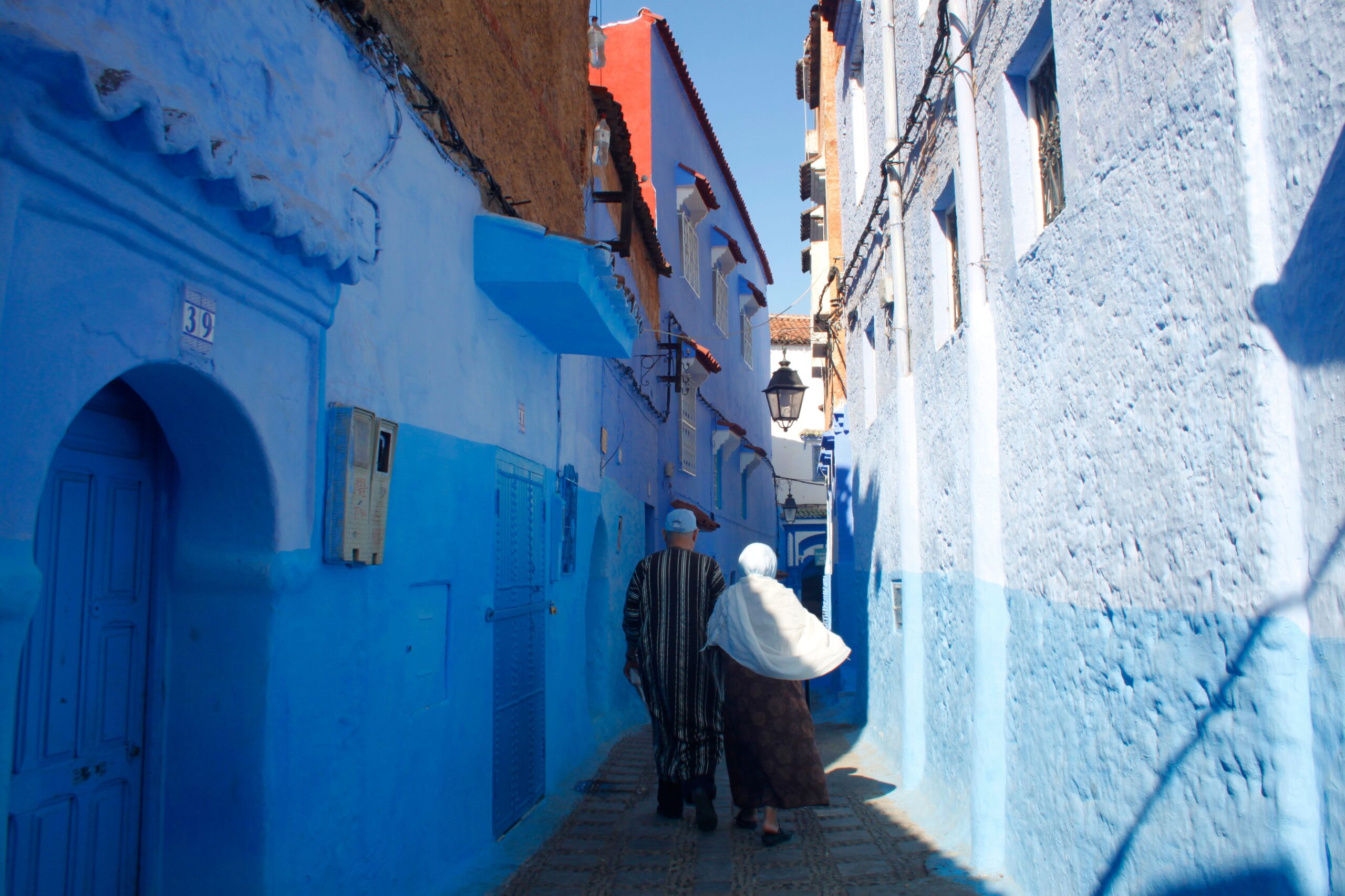 A couple walks through the vibrant blue-painted alleyways of Chefchaouen Morocco under the midday sun