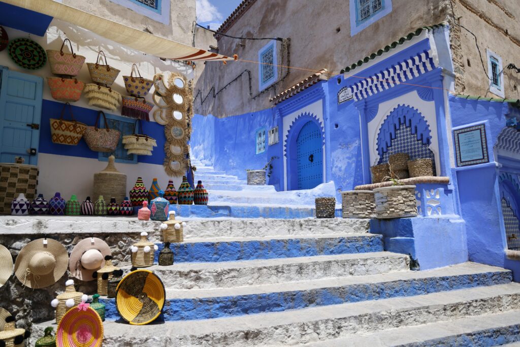 Colorful market scene with traditional Moroccan architecture and merchandise on display in a sunlit alley.