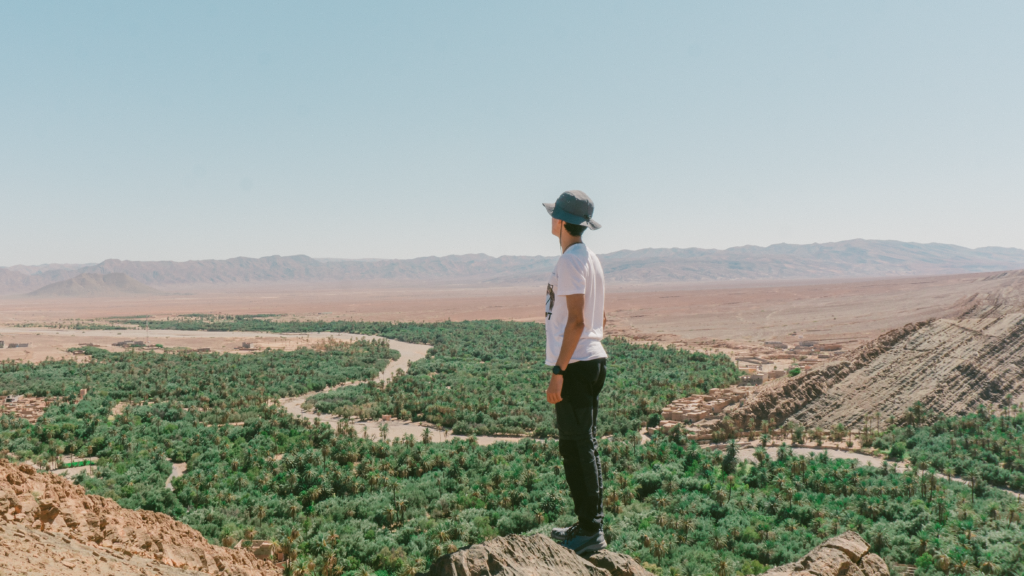 A man stands on a rock, gazing over a lush oasis in Tata, Morocco.